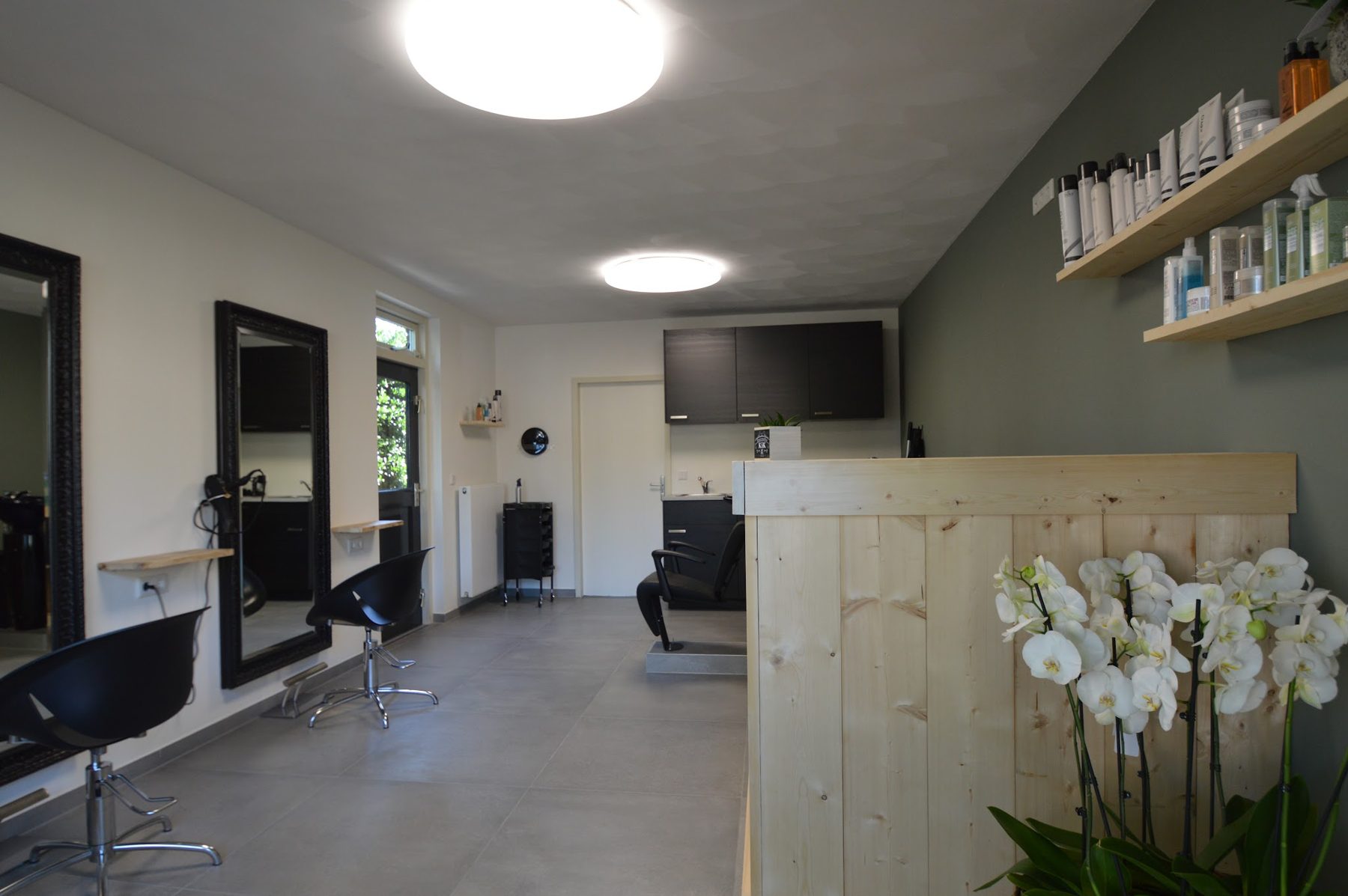 Kappersstoelen voor zwarte spiegels en de houten balie met orchideeën bij Haarstudio KiK