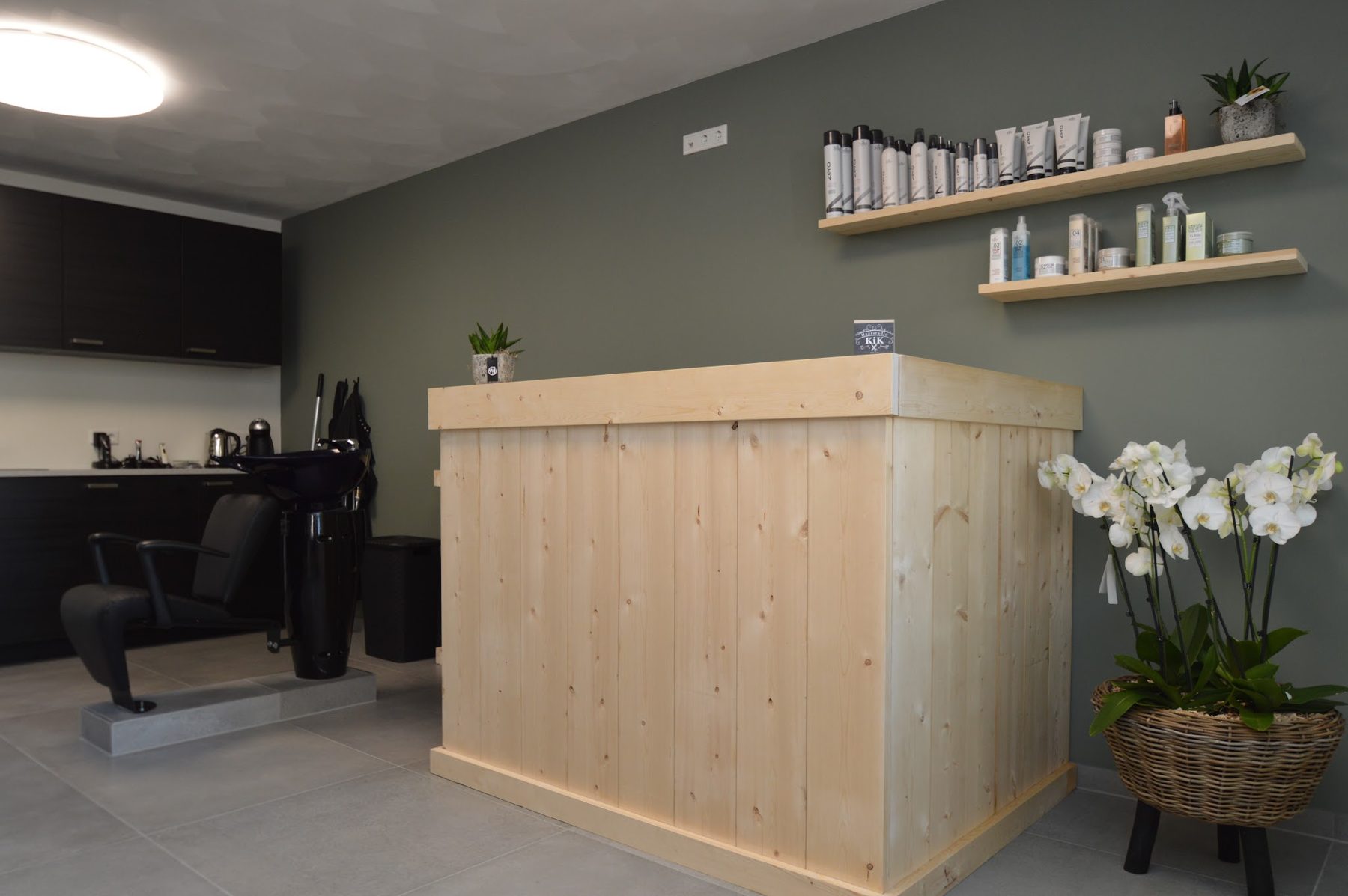 De houten balie van Haarstudio KiK met witte orchideeën en planken met haarproducten tegen de groene wand